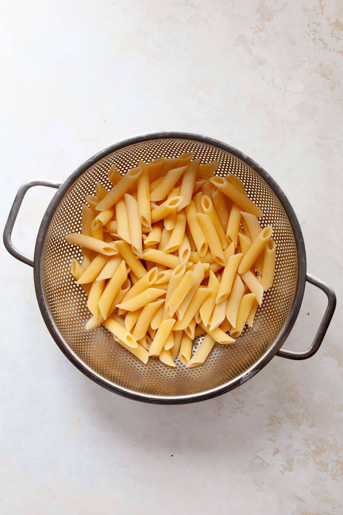 Cooked penne pasta draining in a colander, ready for vodka sauce.