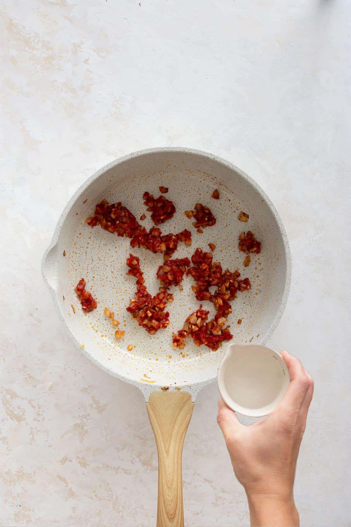 Toasted tomato paste being deglazed with vodka in a skillet.