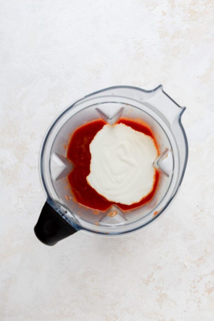 adding Greek yogurt and vodka pasta sauce to a blender to mix