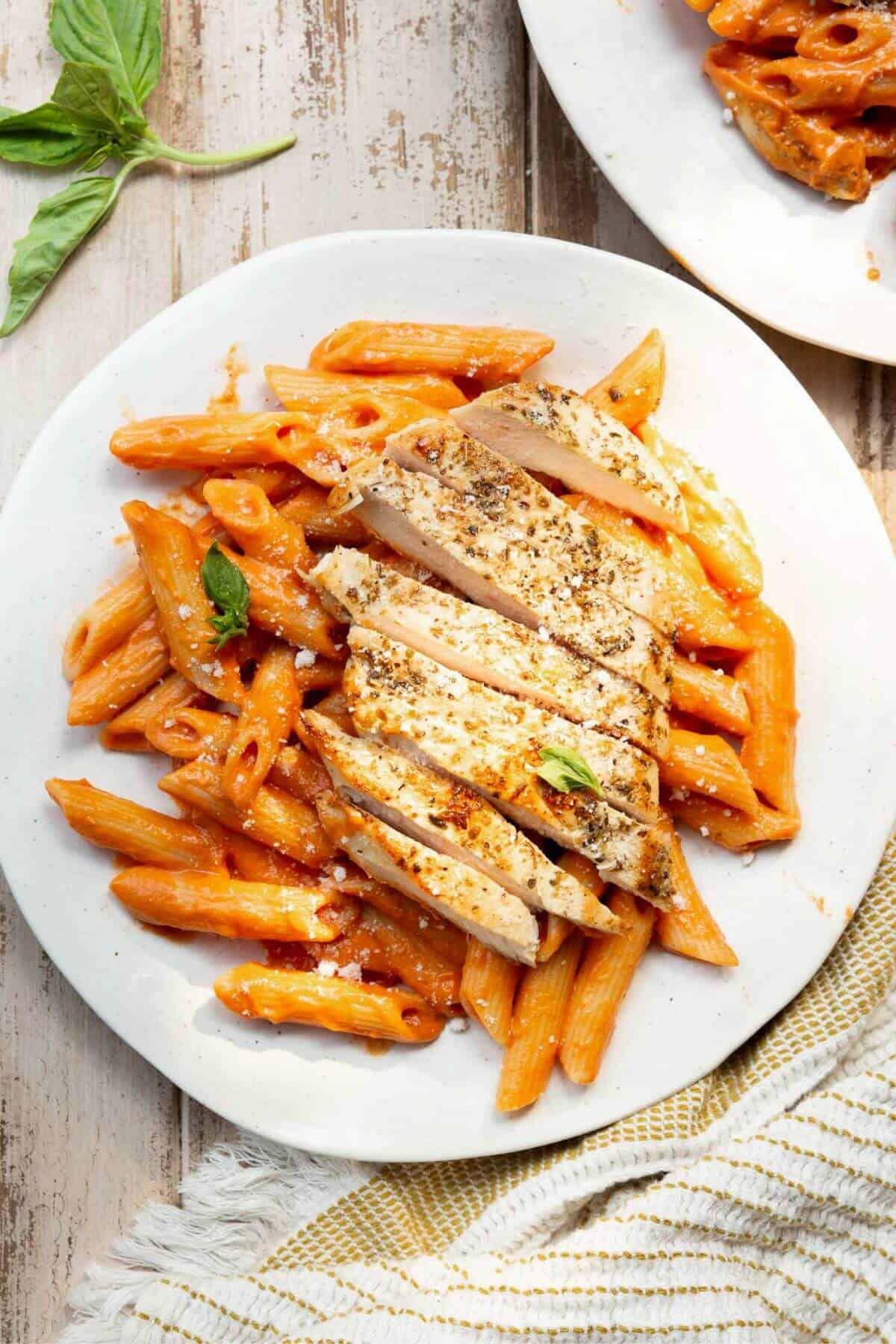 Penne alla vodka with chicken in a creamy blush-orange sauce made without heavy cream, topped with sliced chicken and fresh basil.