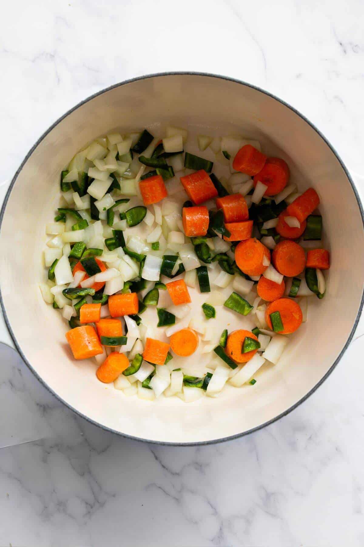 Carrots, poblano pepper, and onion being sautéed in a pot with olive oil until softened.