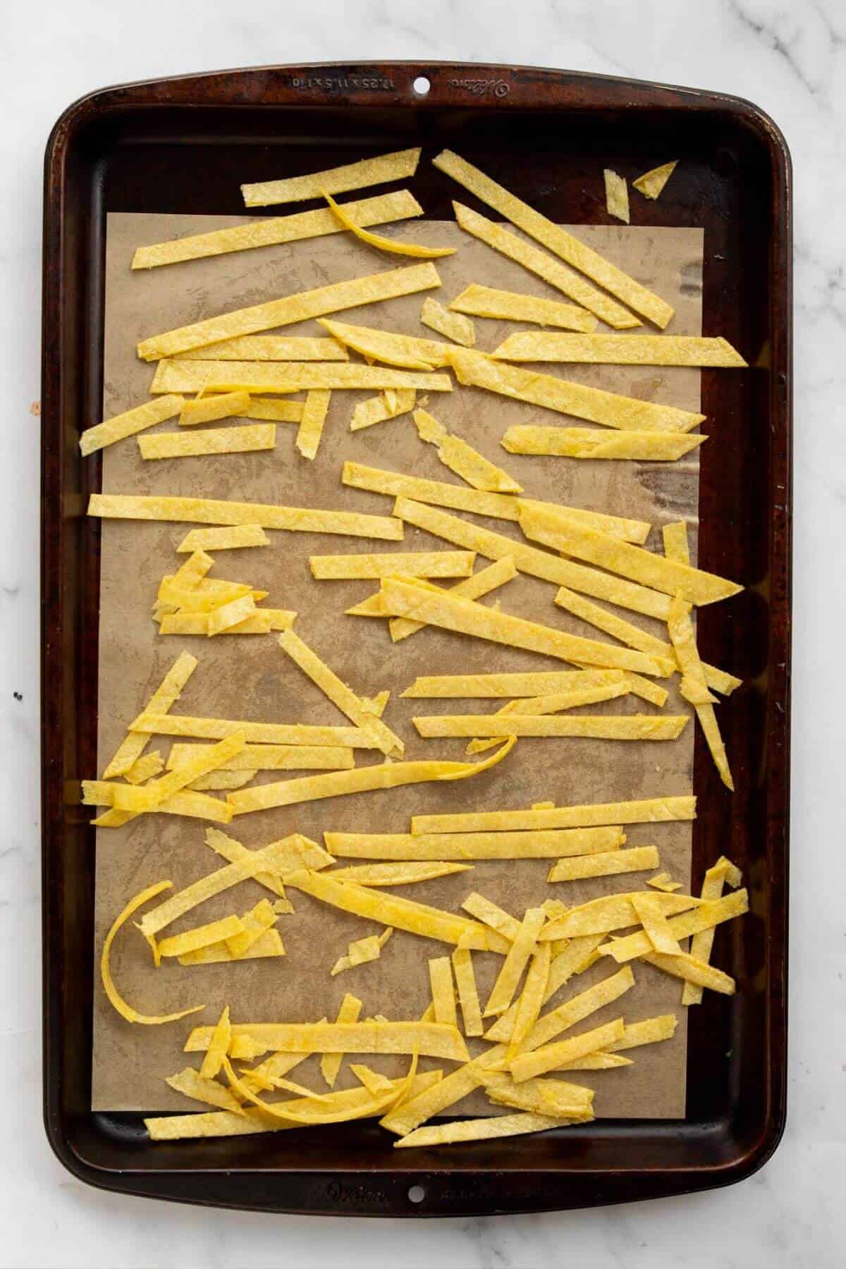 Uncooked tortilla strips spread on a baking sheet before baking for chicken tortilla soup.