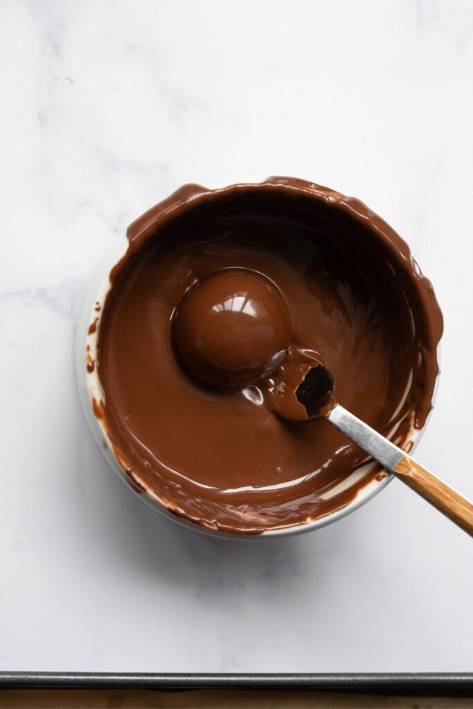 dipping peanut butter ball into melted chocolate an fishing it out with a fork