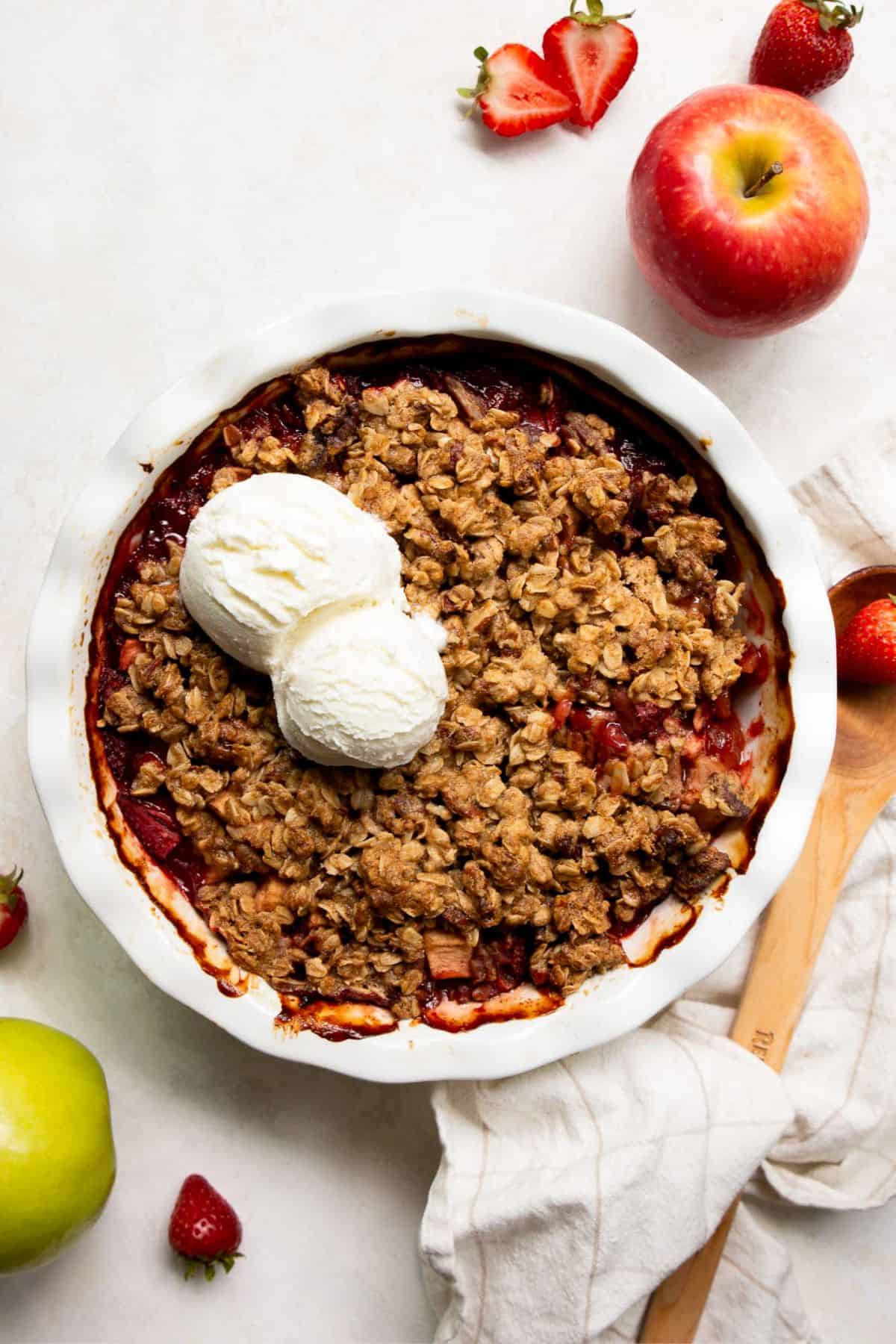 Baked strawberry apple crumble with a scoop of vanilla ice cream melting on top.