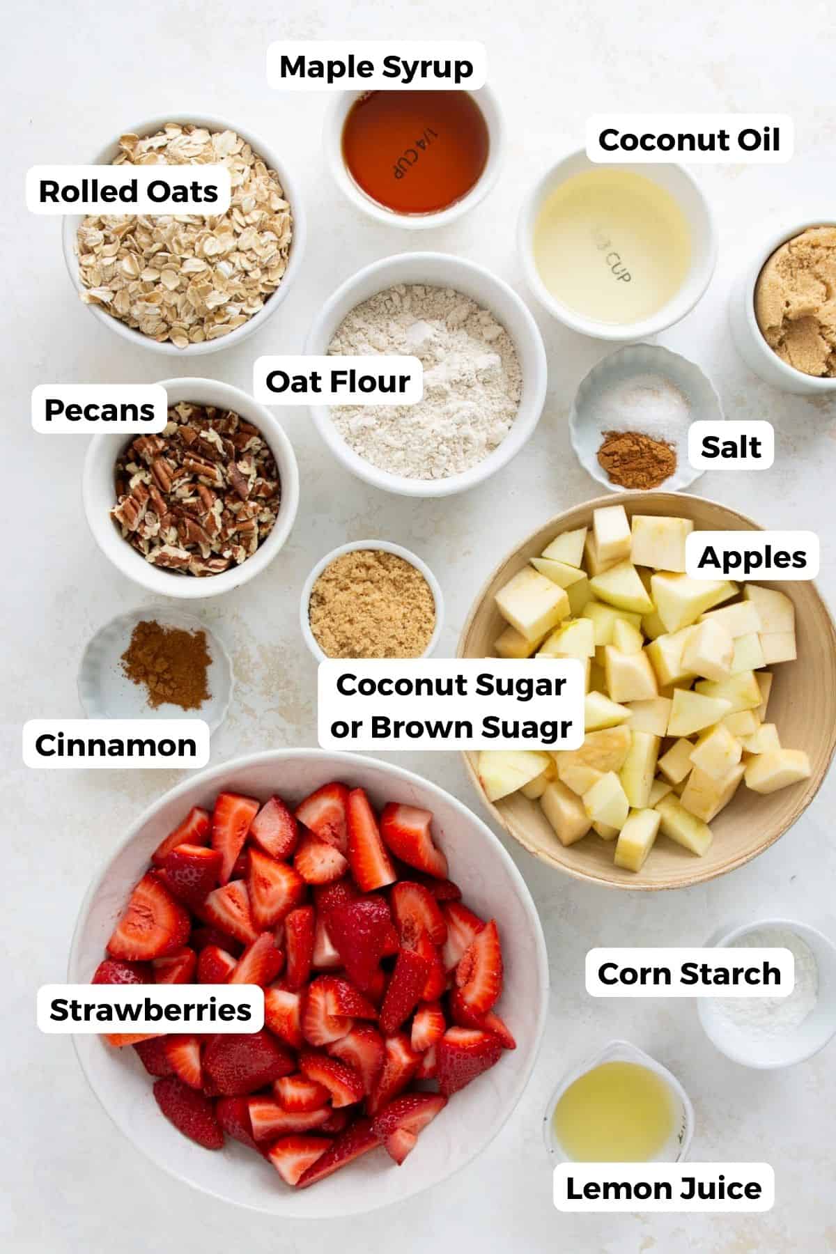 Ingredients for healthy strawberry apple crumble including strawberries, apples, oats, maple syrup, and coconut sugar.