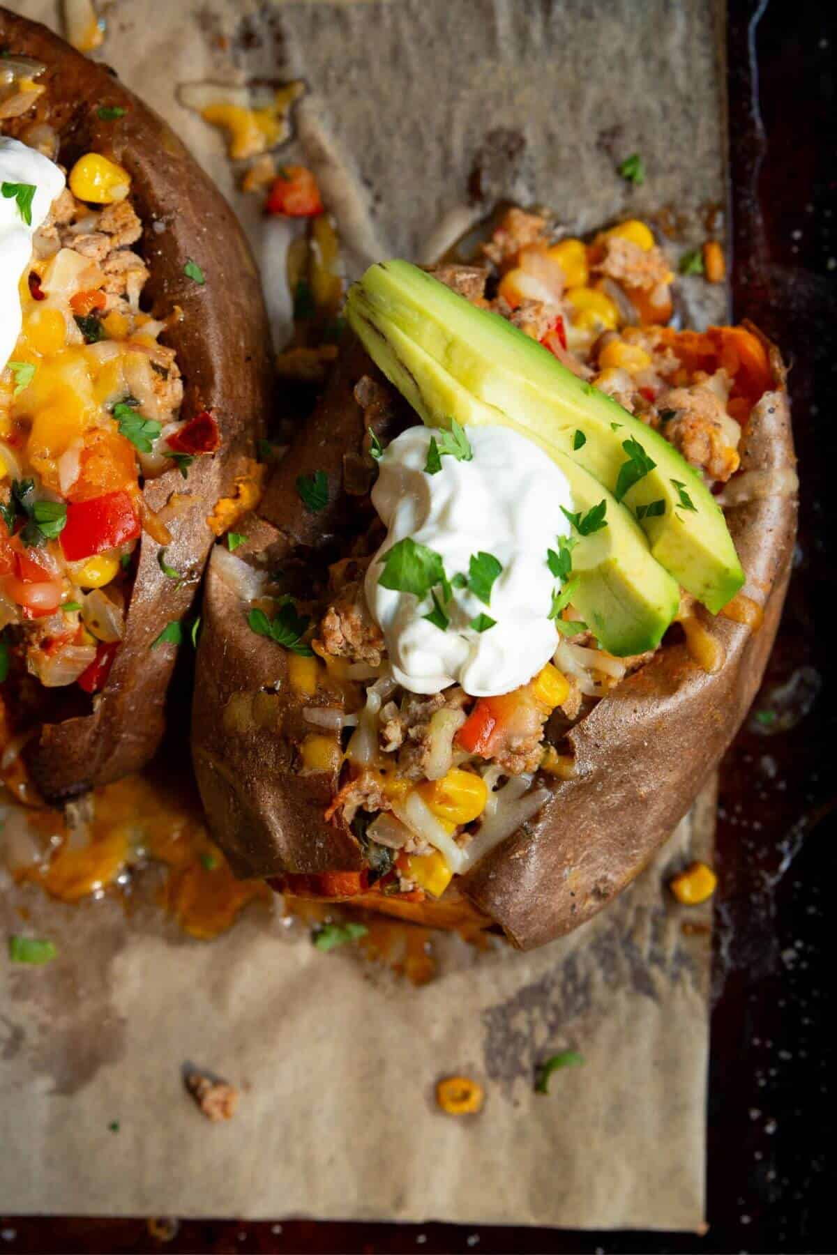 Cheesy turkey taco stuffed sweet potatoes with avocado and sour cream.
