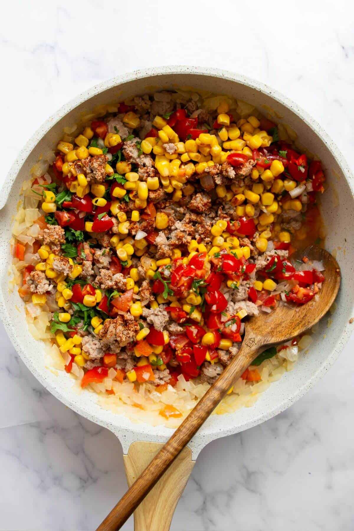 Adding frozen corn and cilantro to ground turkey filling.