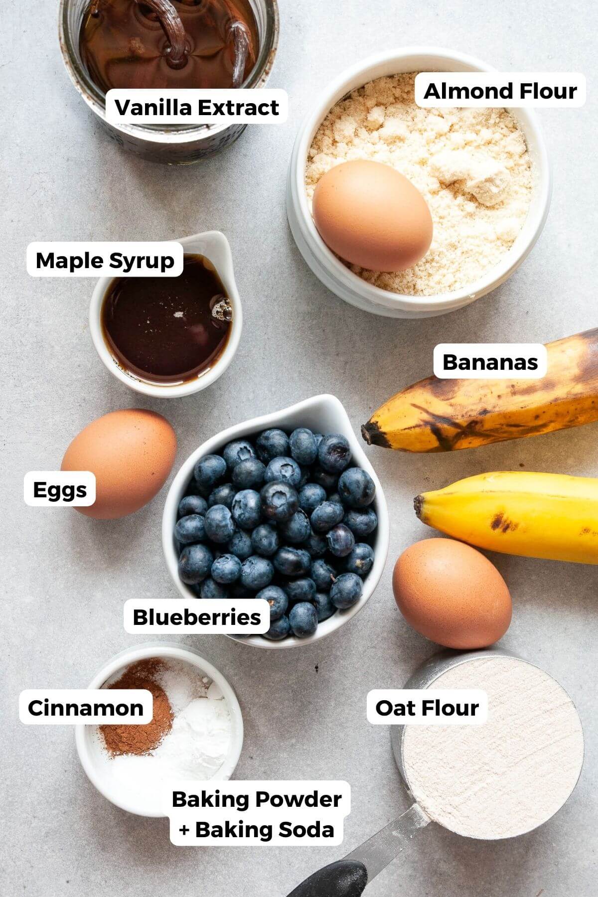 Ingredients for healthy blueberry banana bread including almond flour, oat flour, ripe bananas, eggs, maple syrup, and fresh blueberries.
