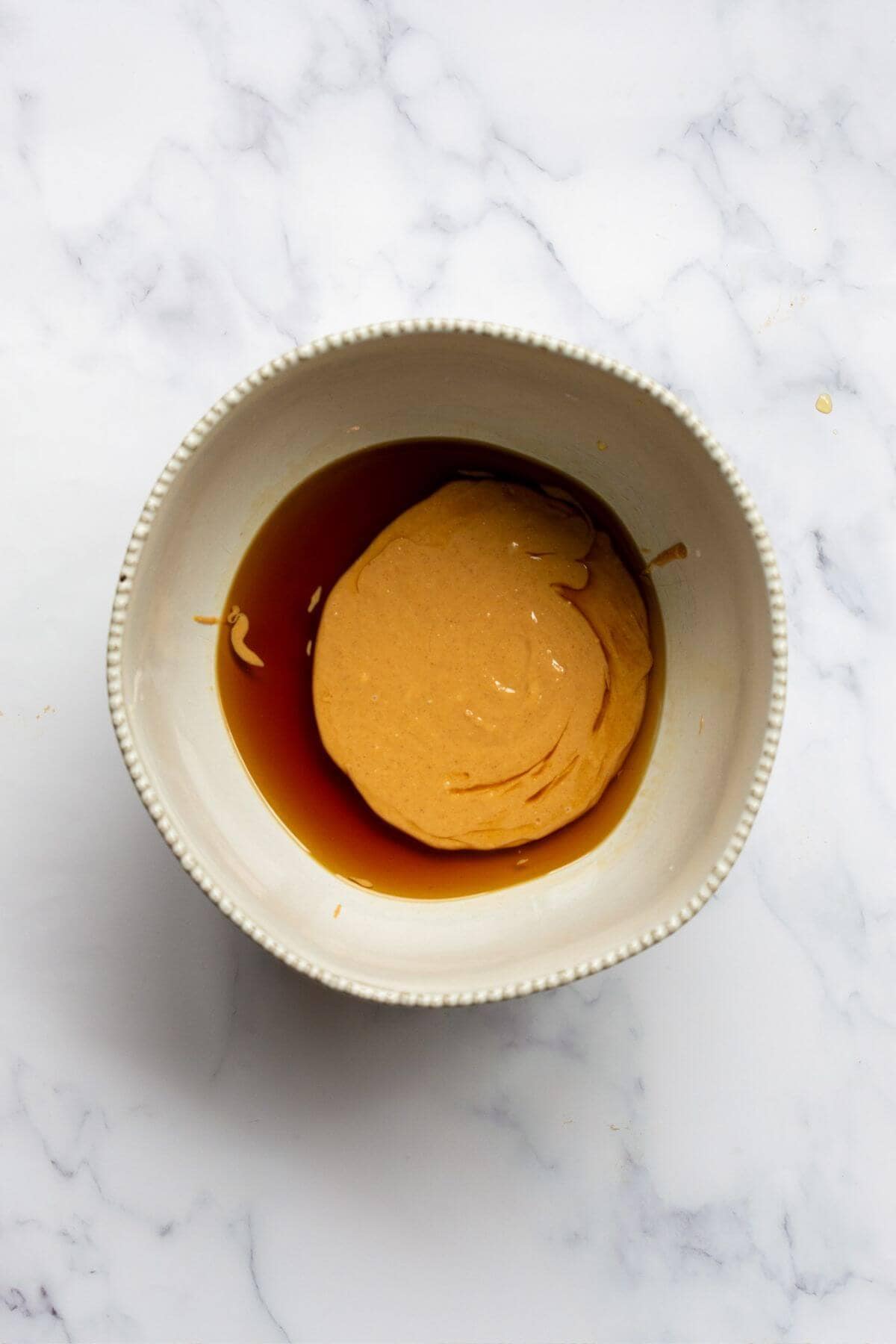 Peanut butter, maple syrup, and vanilla extract in a small white bowl before being added to the oats.