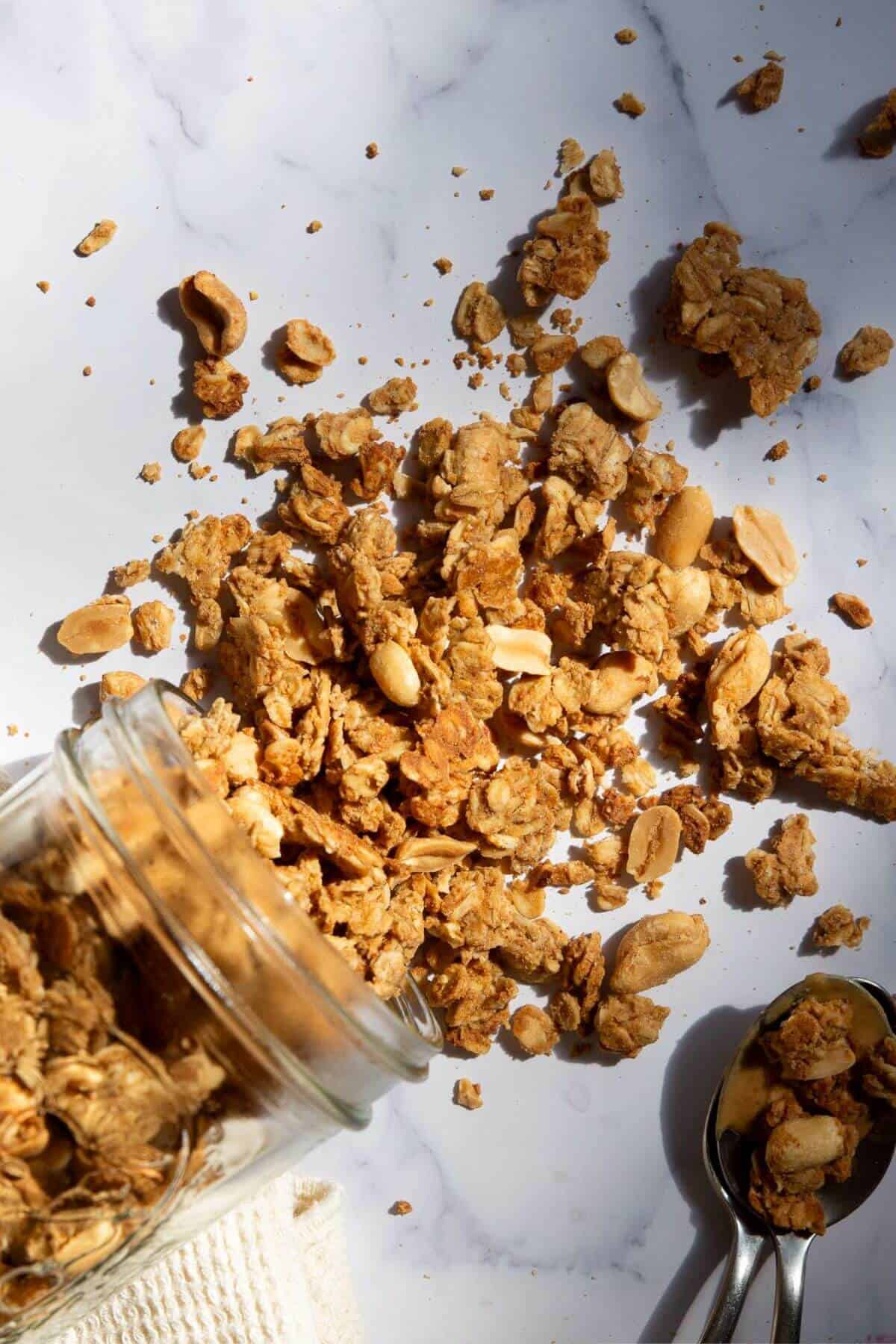 Close up of chunky homemade peanut butter granola clusters spilling out of a glass mason jar.