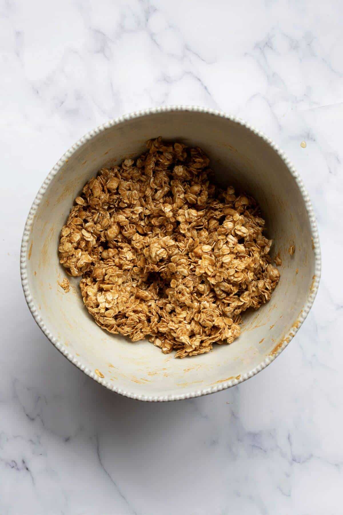 Peanut butter granola mixture fully combined in a mixing bowl with every oat coated in the maple peanut butter binder.