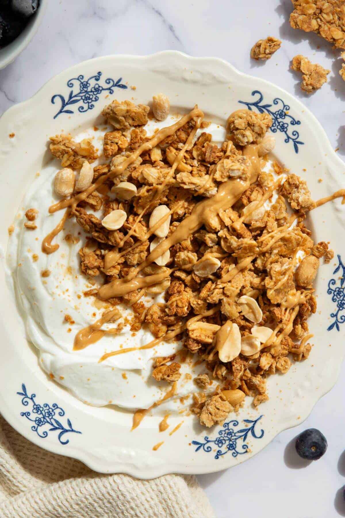 Bowl of chunky homemade peanut butter granola served over Greek yogurt with fresh blueberries and a drizzle of peanut butter.