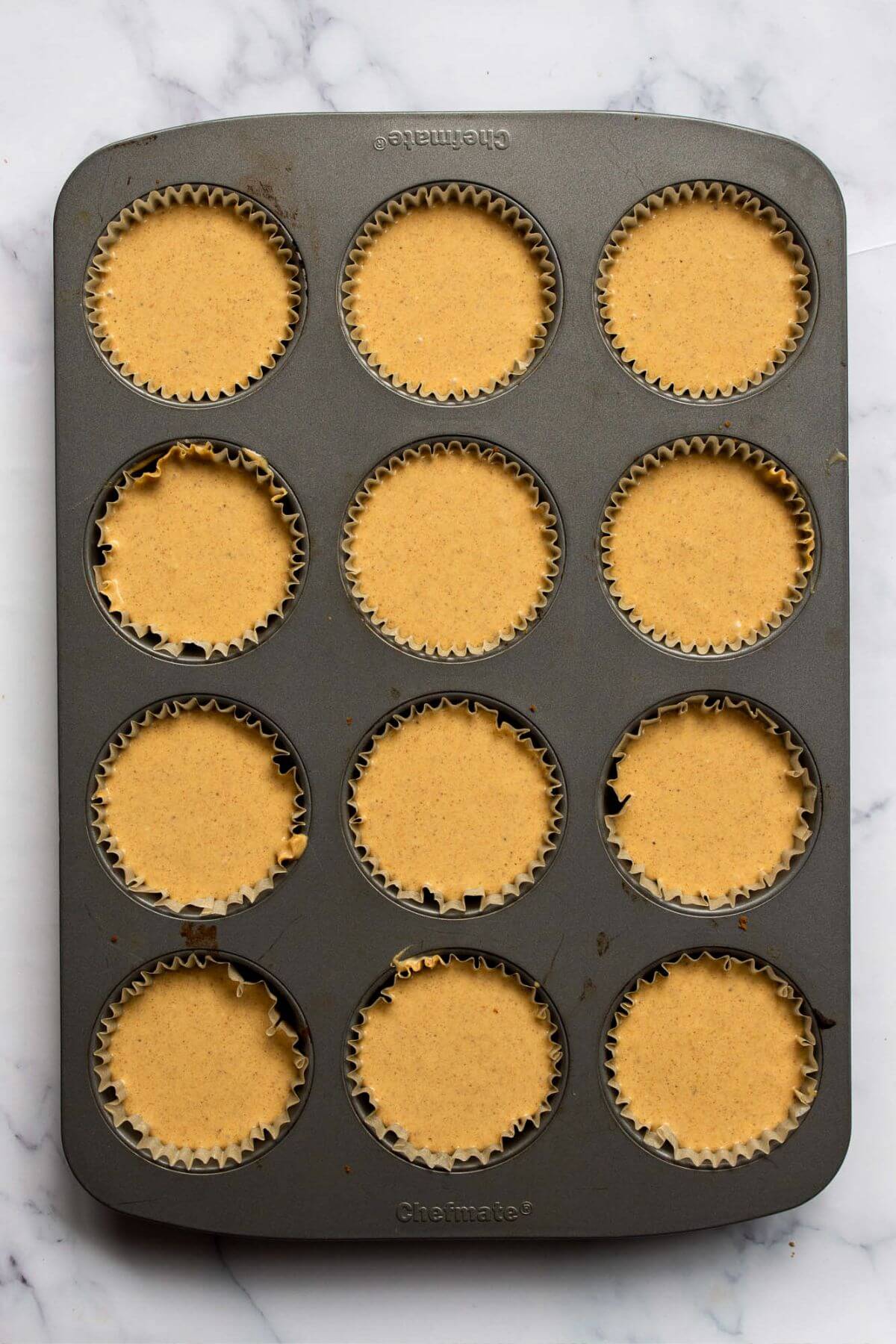 Healthy pumpkin cheesecake batter divided into 12 mini bites unbaked in a muffin tin.
