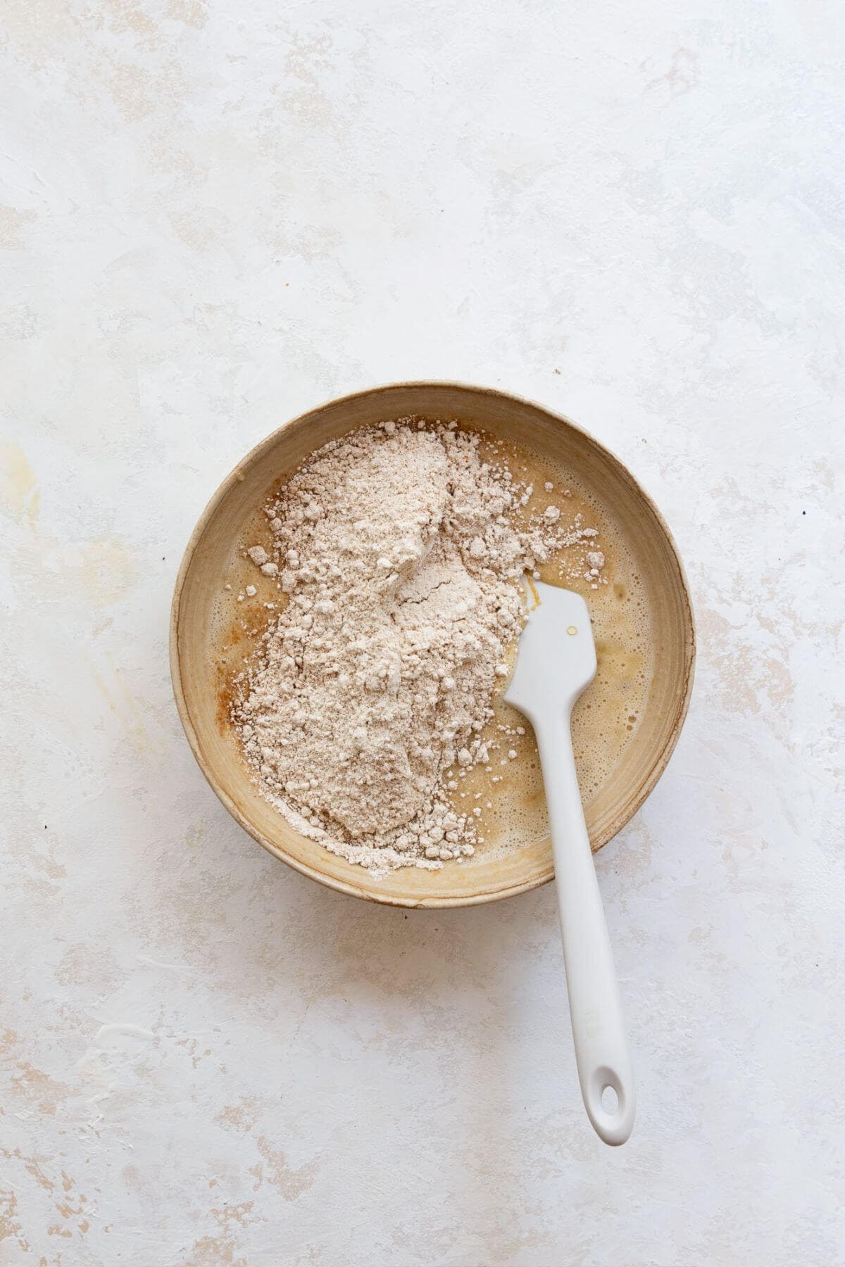 Oat flour and baking powder added to wet banana bread batter in a bowl.
