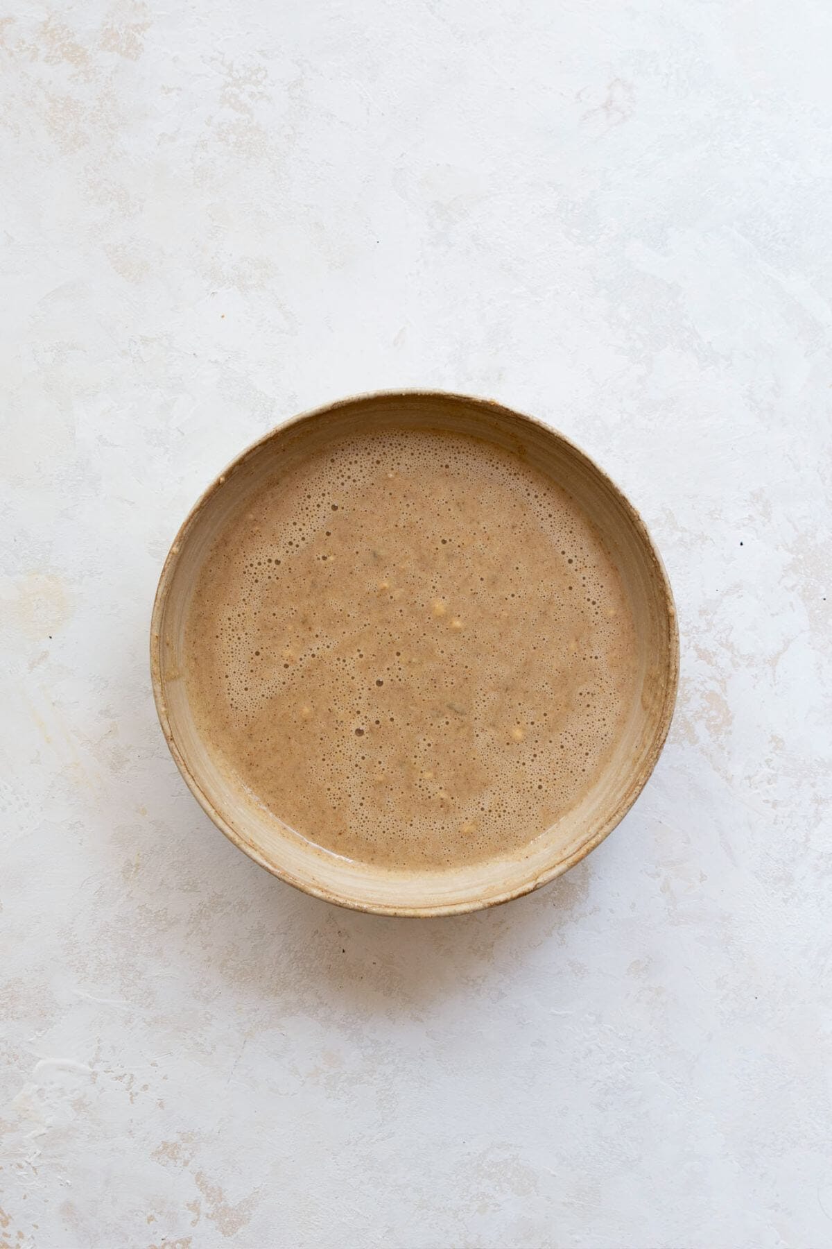 Wet ingredients for single serve banana bread whisked together in a small bowl, including mashed banana, egg, milk, maple syrup, and nut butter.