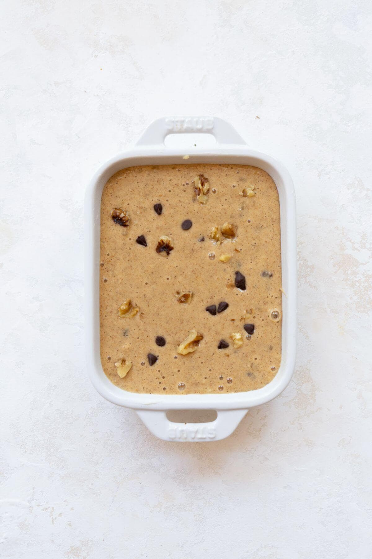 Single serve banana bread batter in a white ramekin, topped with chocolate chips and walnuts before baking.