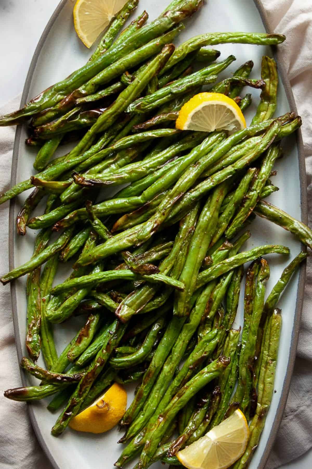 Air fryer green beans served on a platter with fresh lemon wedges.