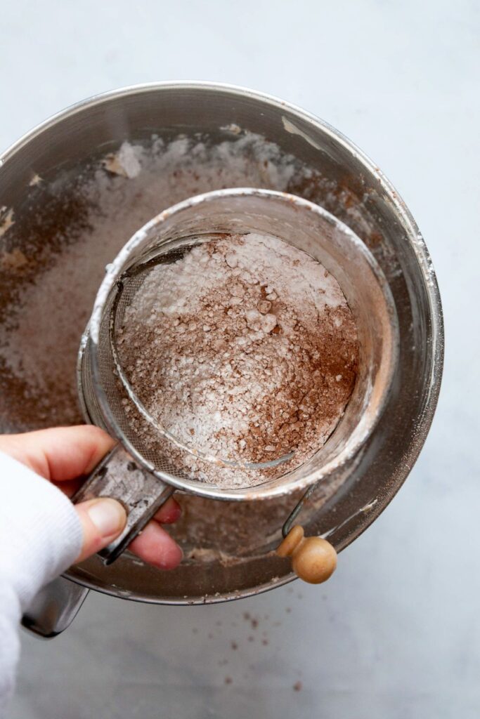 sifting powdered sugar and cocoa powder into mixing bowl to form buttercream