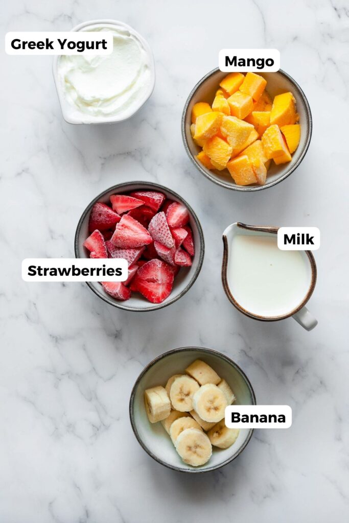 all five ingredients in this banana mango strawberry smoothie in small bowls with labels