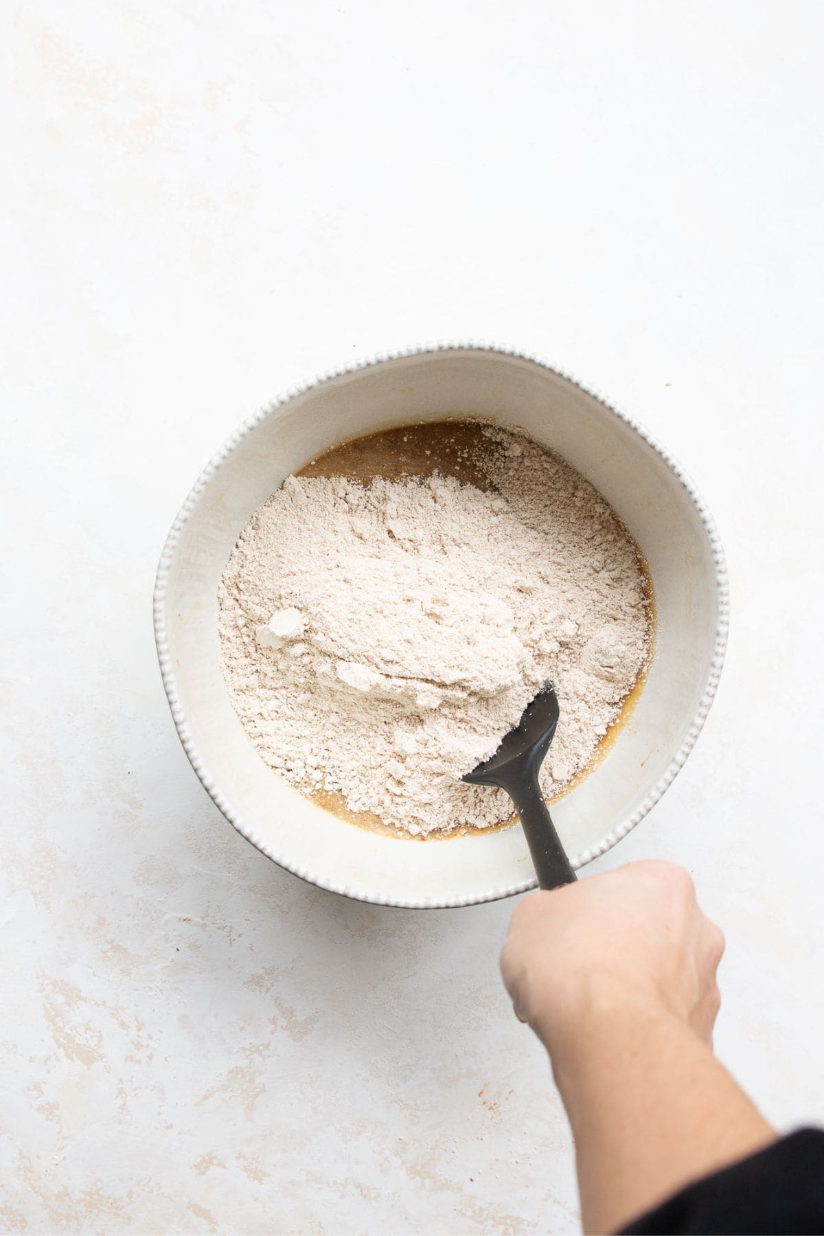 Oat flour being folded into banana blueberry oatmeal muffin batter in a white bowl.