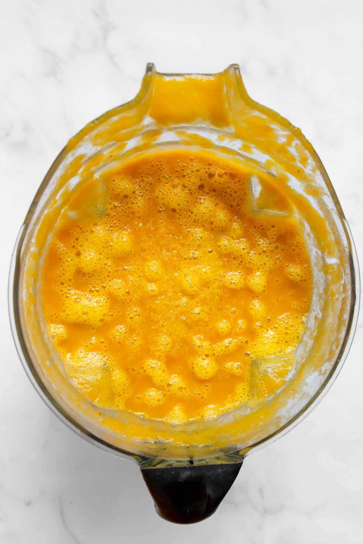 Cooked butternut squash and carrot soup being blended in a high-speed blender until smooth and creamy.