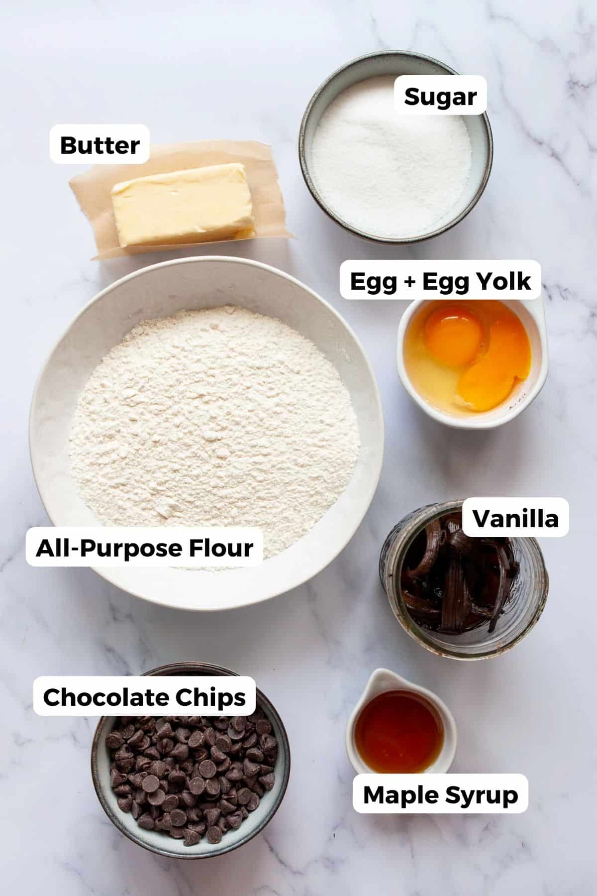 Ingredients for chocolate chip cookies without brown sugar: butter, sugar, egg and yolk, flour, vanilla, chocolate chips, and maple syrup.