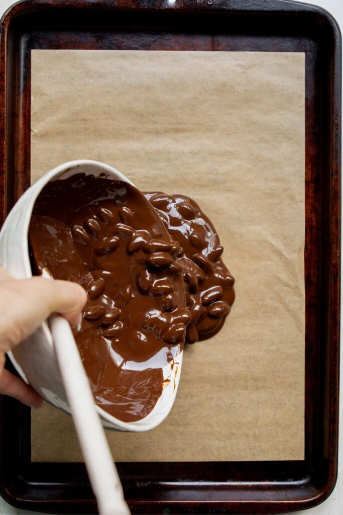 pouring melted chocolate with almonds in it onto a baking sheet