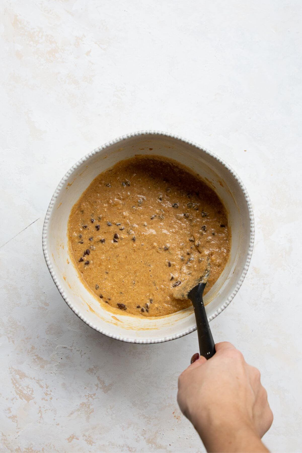 Folding chocolate chips into oat flour banana bread batter.