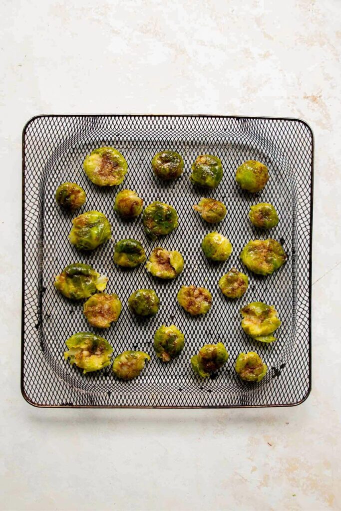 adding uncooked smashed Brussels sprouts to an air fryer basket