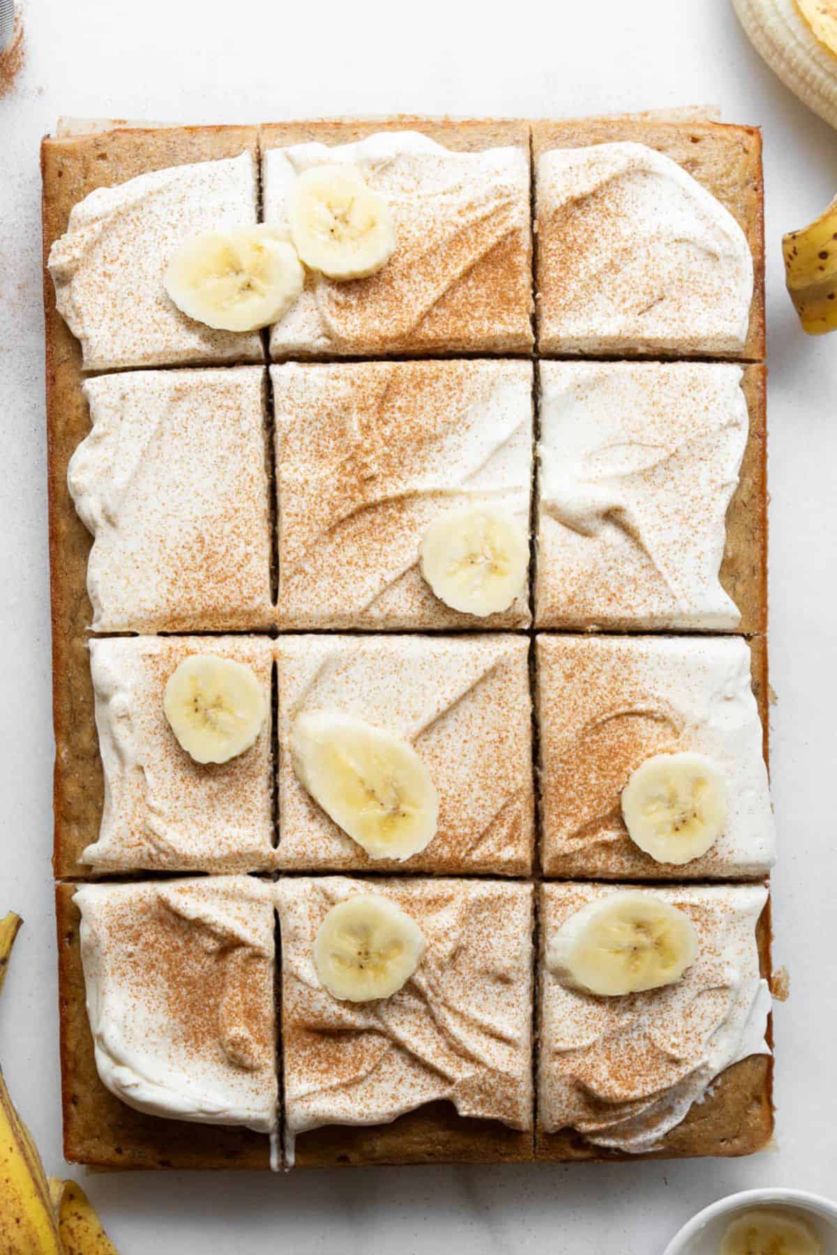 Frosting and decorating gluten-free banana cake with fresh banana slices and cream cheese frostin.