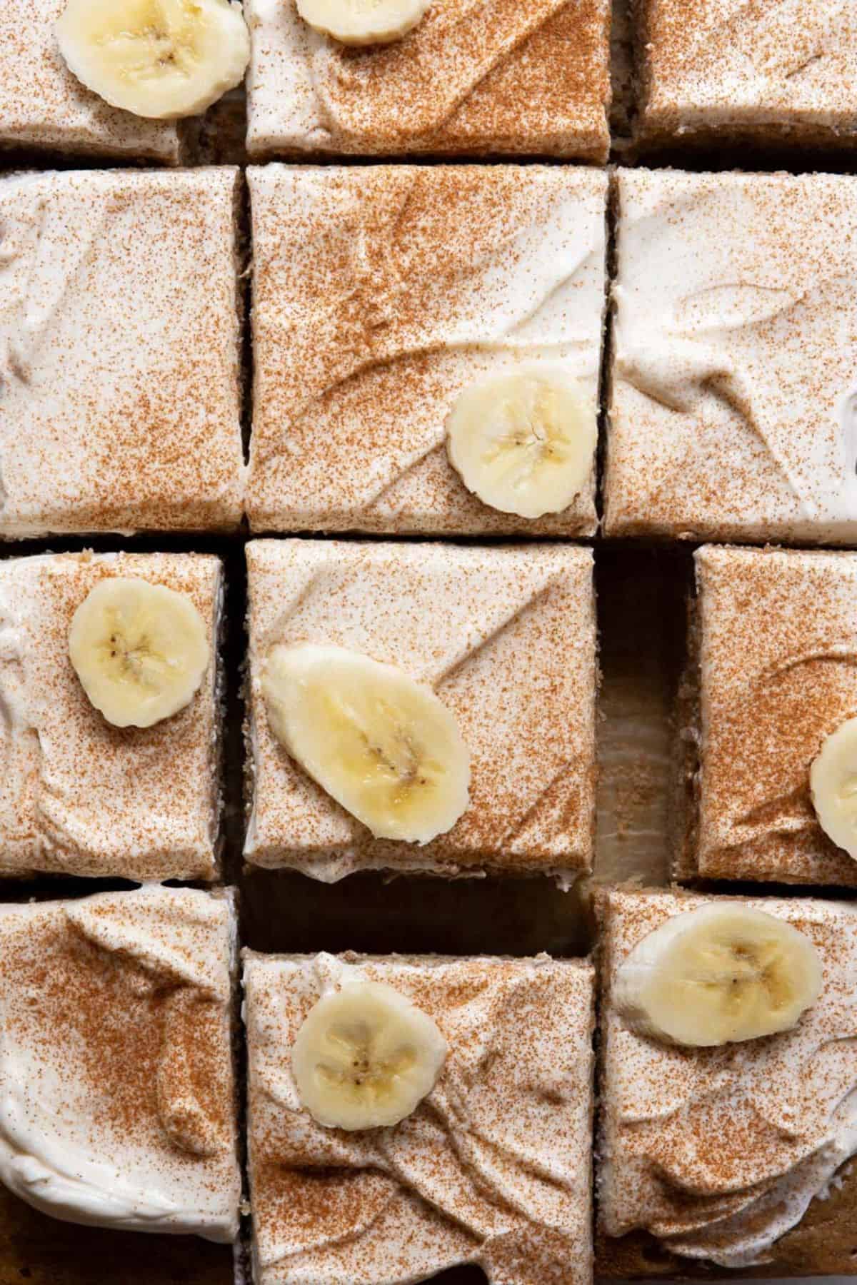 Slices of gluten-free banana cake topped with maple cream cheese yogurt frosting and fresh banana slices.