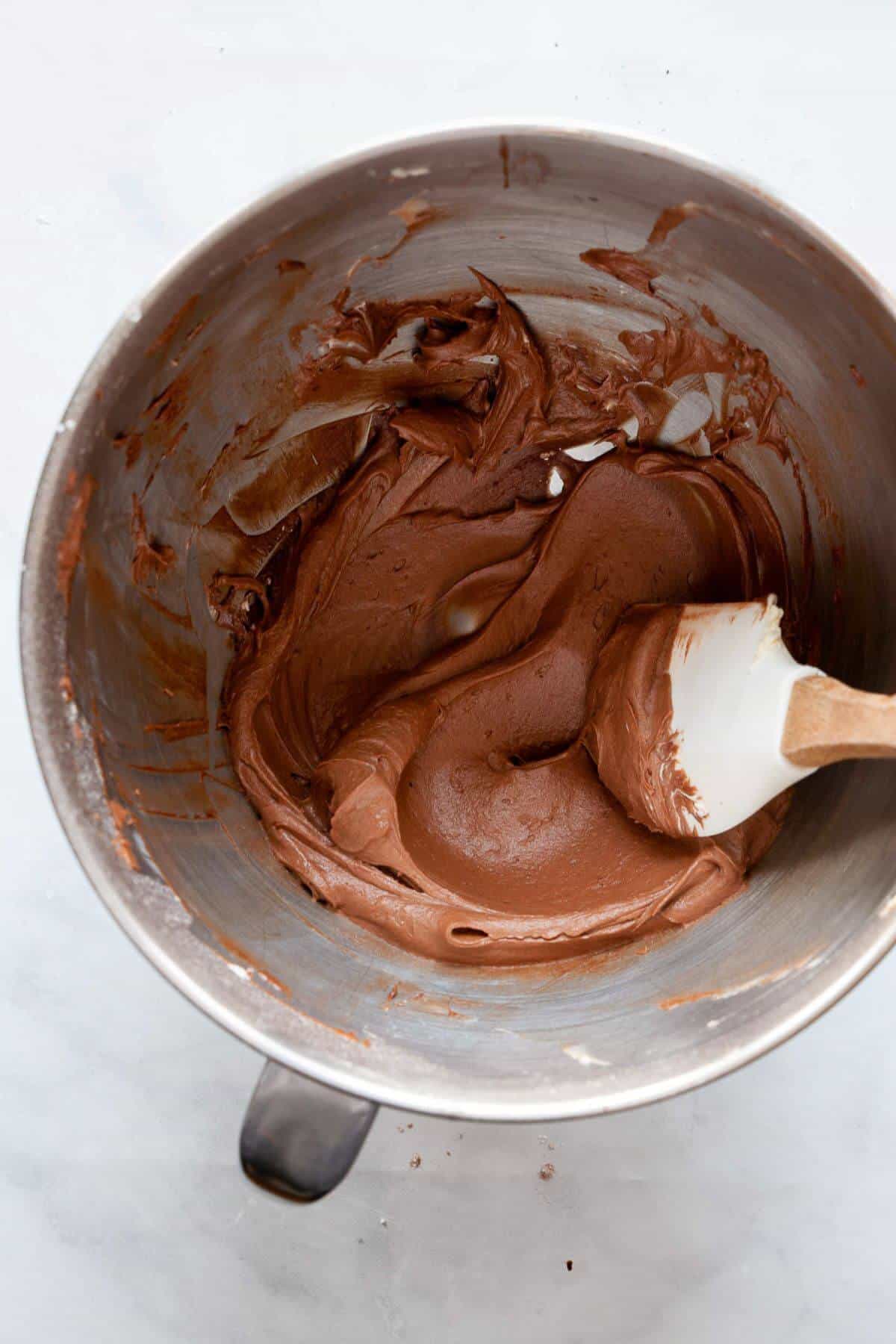Dairy-free chocolate buttercream frosting being mixed with a spatula.