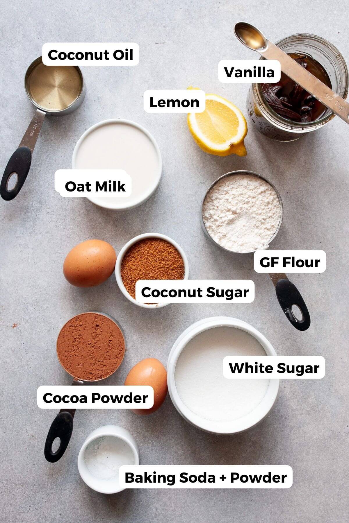 Ingredients for gluten-free chocolate cupcakes including cocoa powder, coconut sugar, coconut oil, oat milk, gluten-free flour, eggs, and lemon.