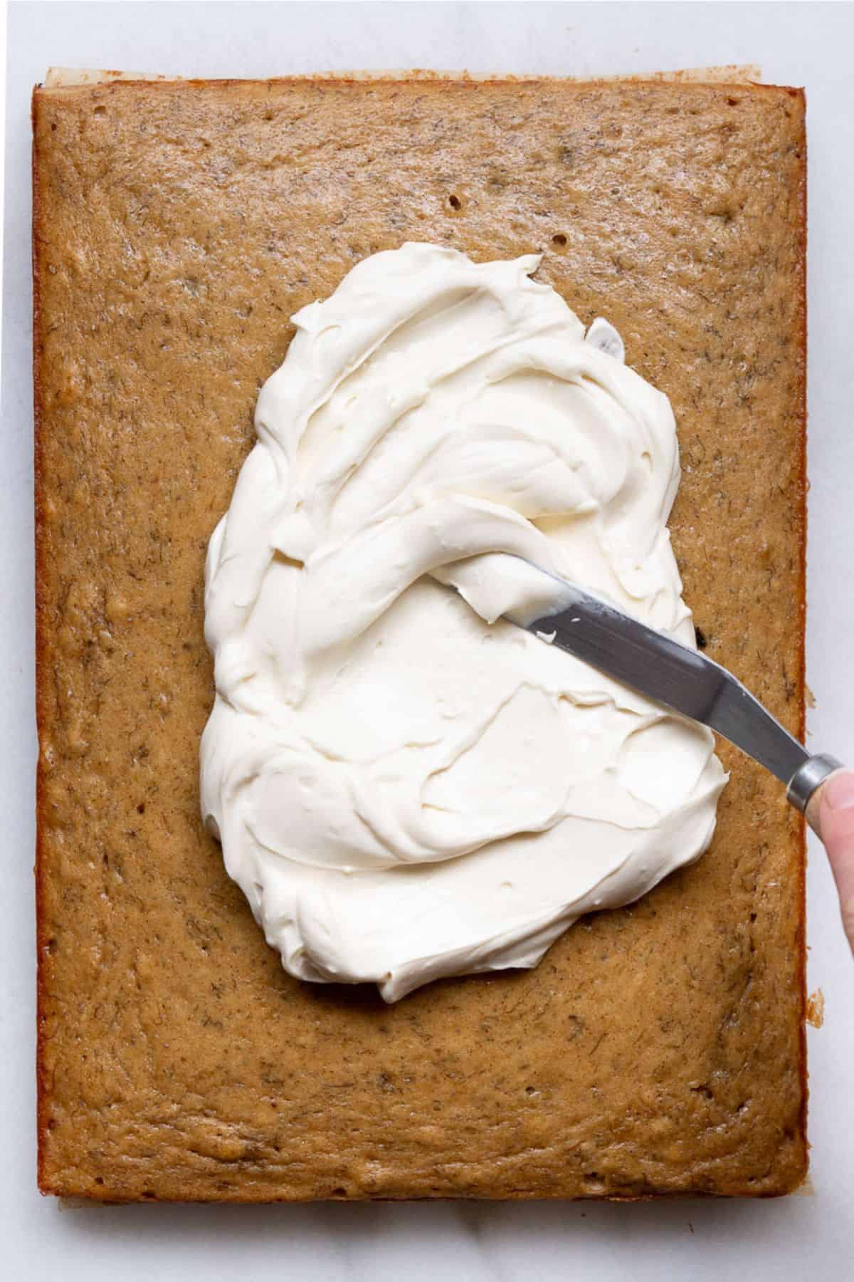 Spreading maple cream cheese yogurt frosting onto a cooled gluten-free banana cake in a 9x13 pan.