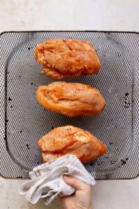 adding raw chicken marinated in buffalo sauce to an air fryer basket
