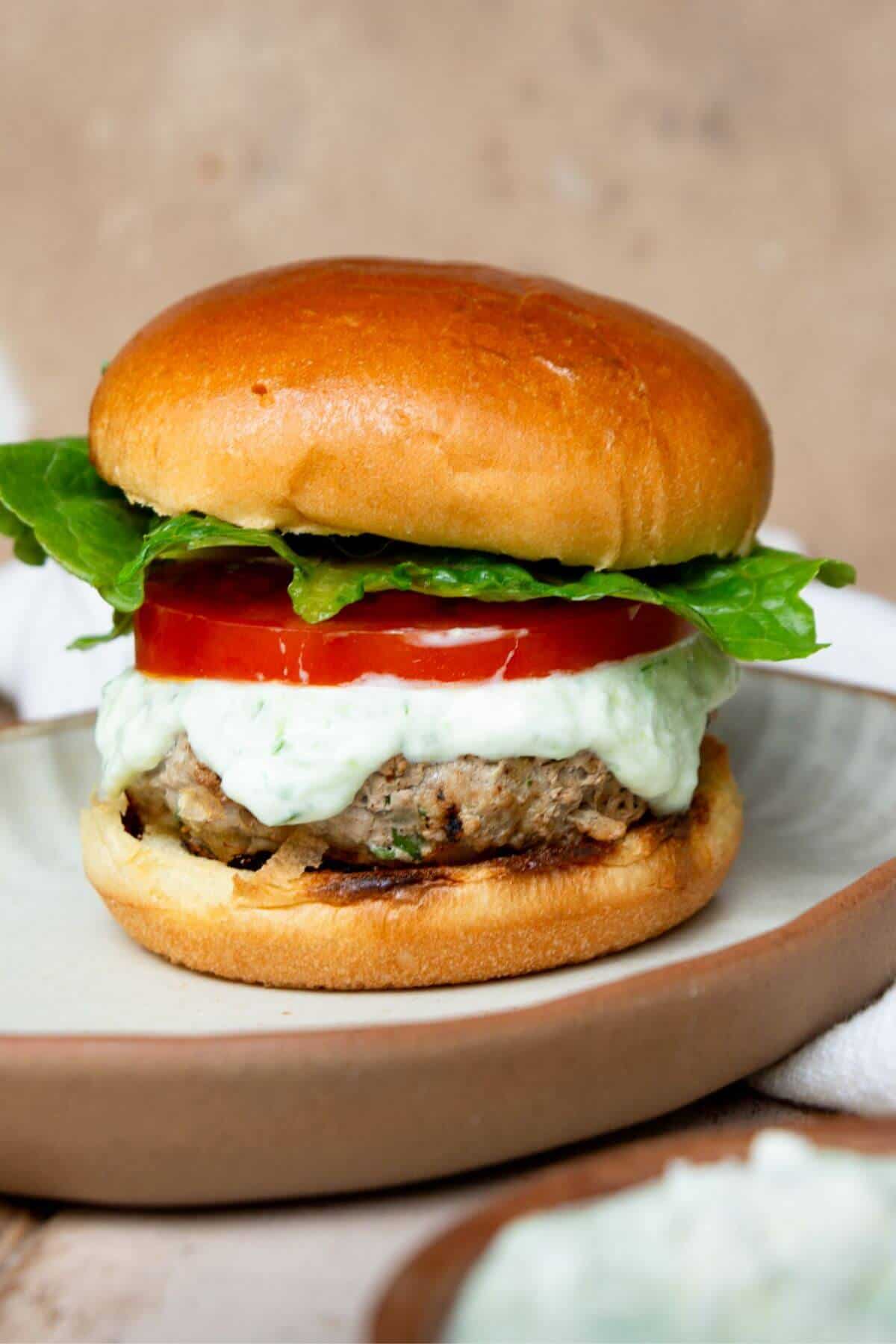 Greek turkey burger with feta topped with tzatziki, tomato, and lettuce on a toasted bun.