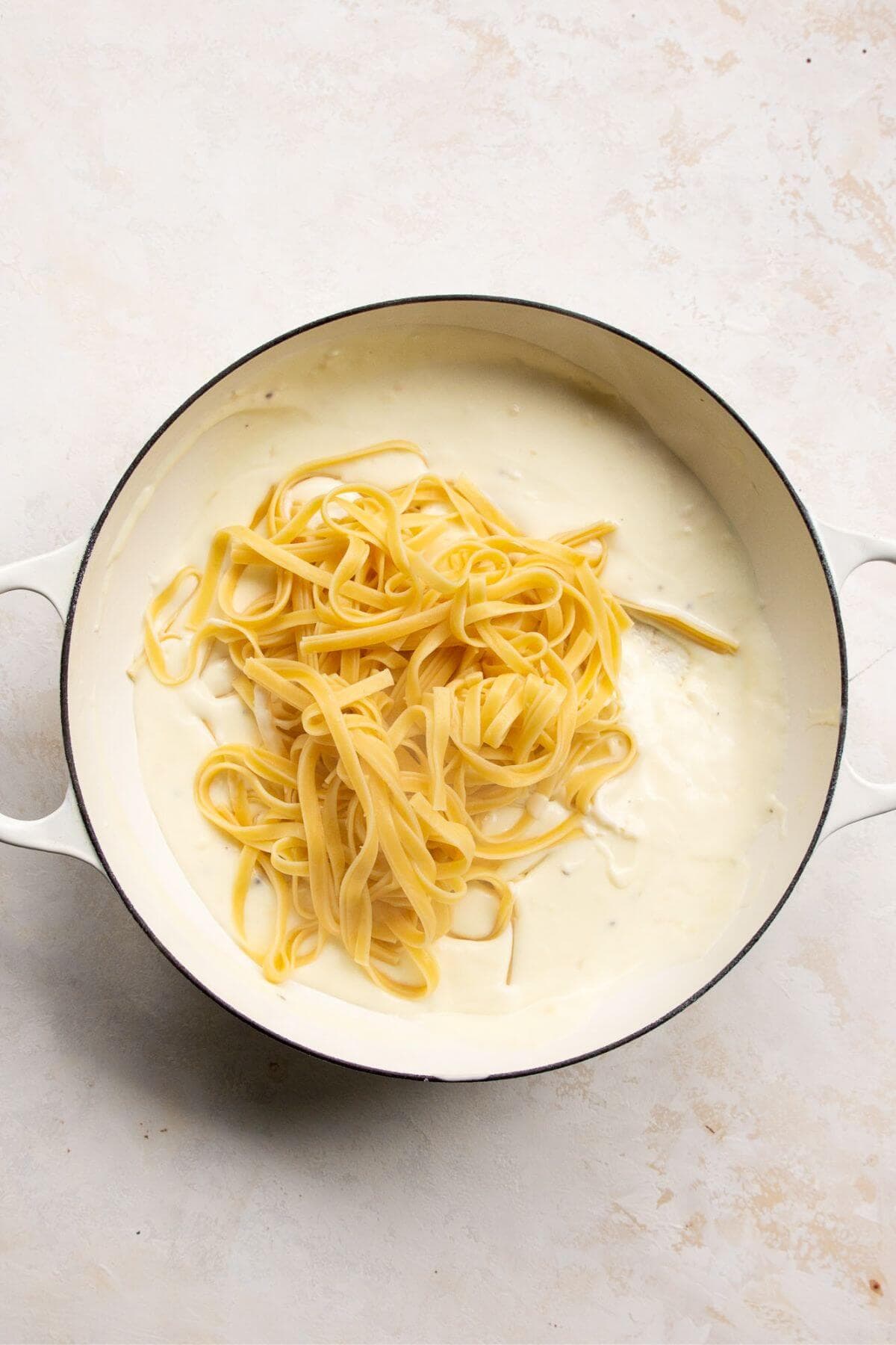 Adding cooked fettuccine pasta to Healthy Alfredo Sauce in a pot.