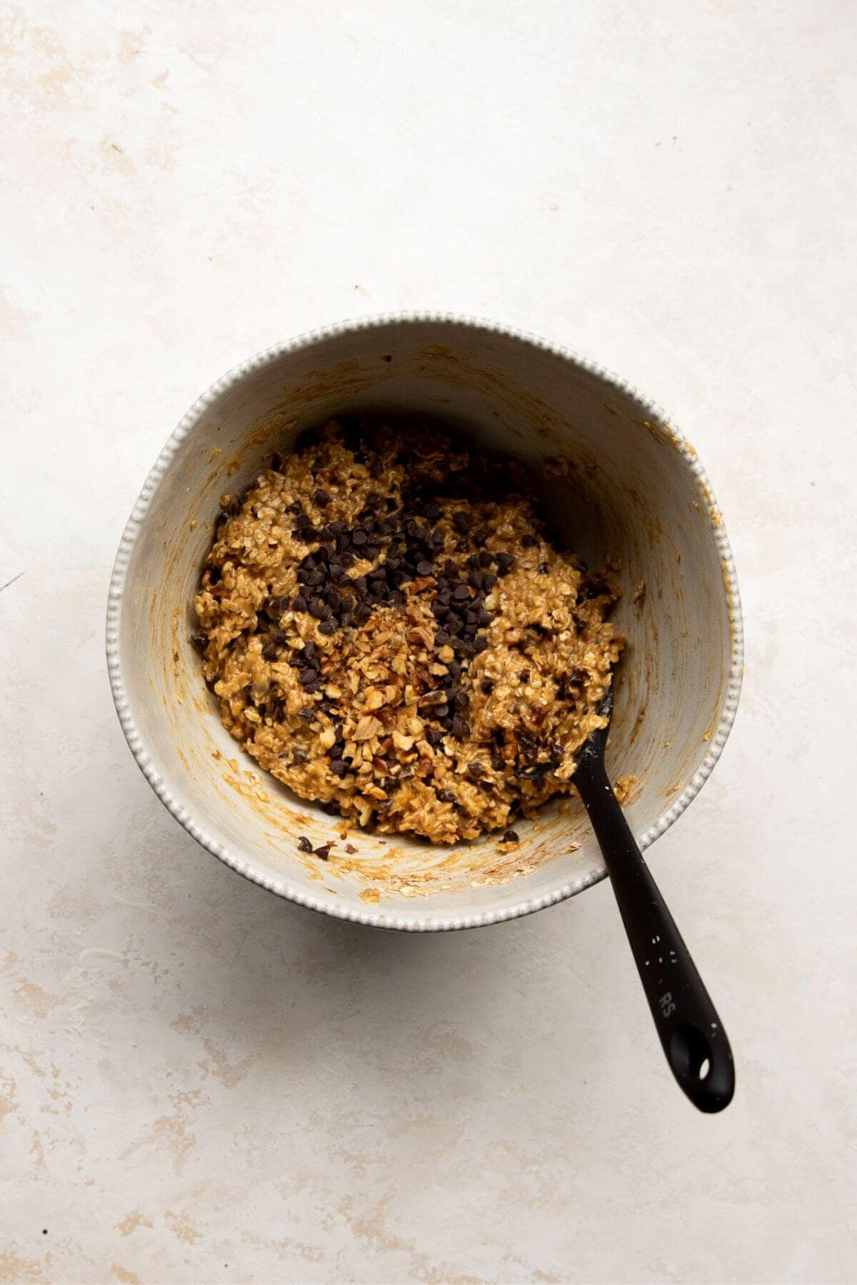 Banana oat breakfast cookie batter in a mixing bowl with oats and mashed bananas combined.