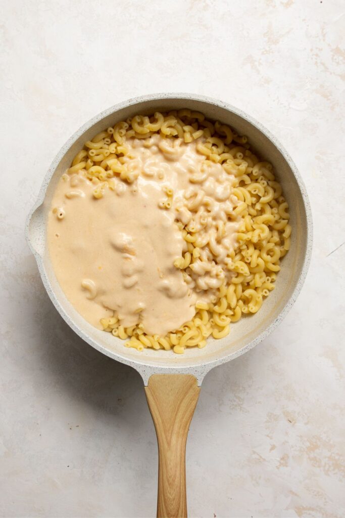 adding cheesy sauce to cooked macaroni