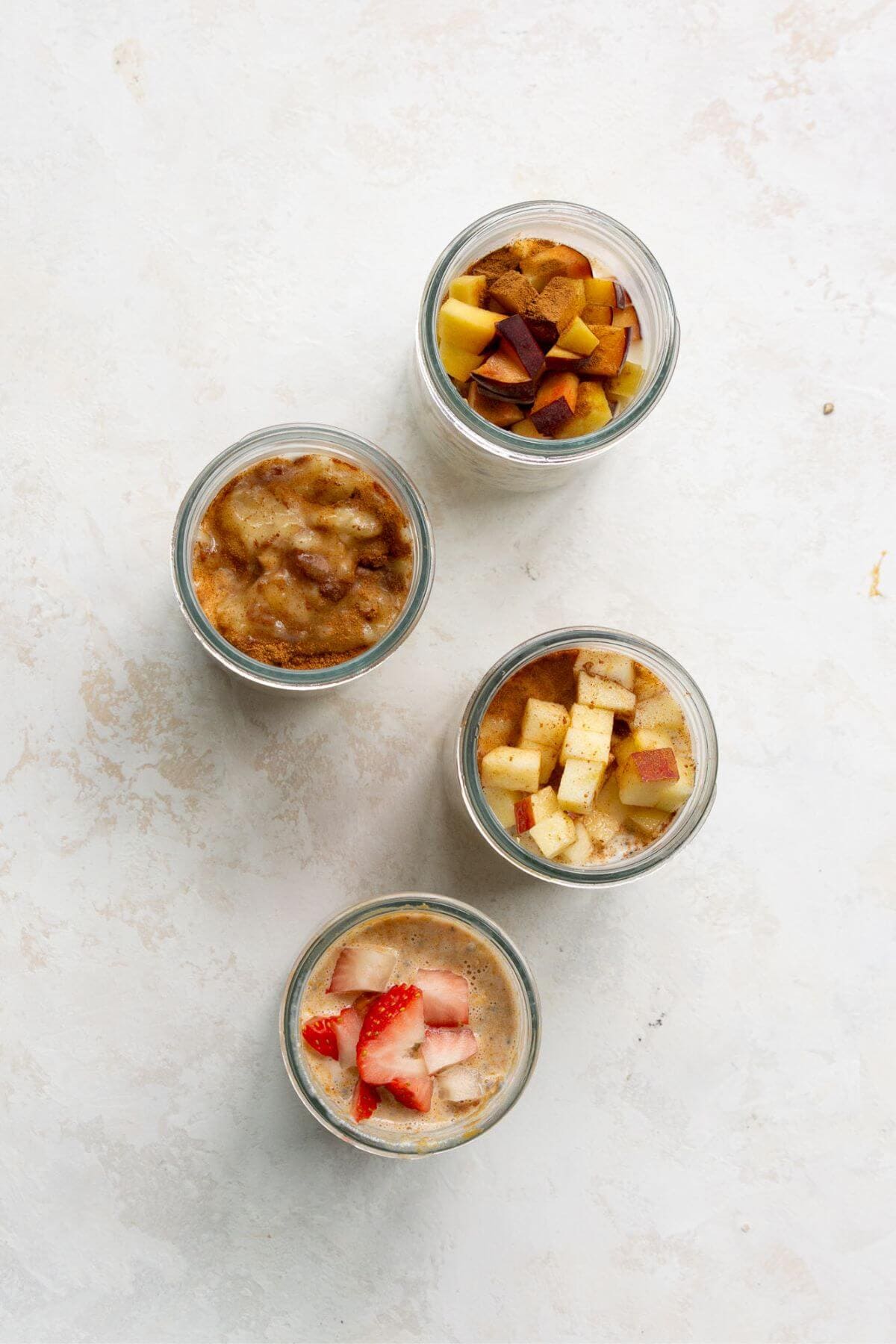 Adding toppings to protein overnight oats base with four total jars with flavors including: pb&J, peaches and cream, apple pie, and banana bread.