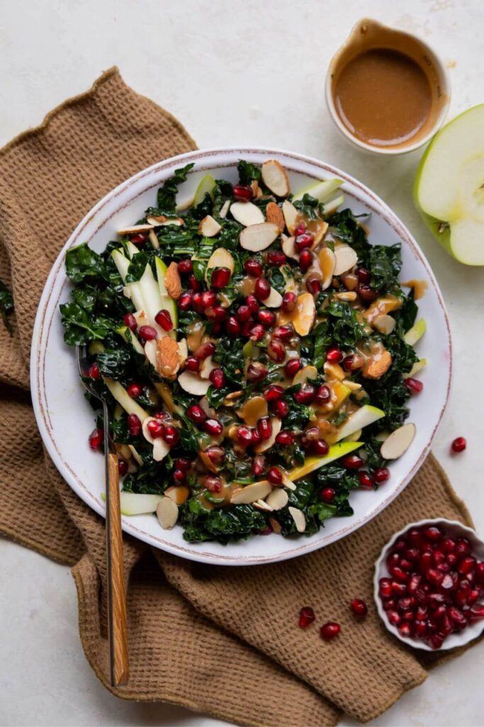 kale pomegranate salad with almonds and green apple on a serving plate