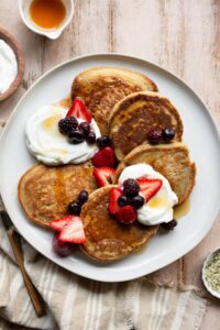 healthy, fluffy oat flour pancakes on a plate with greek yogurt, berries, and syrup