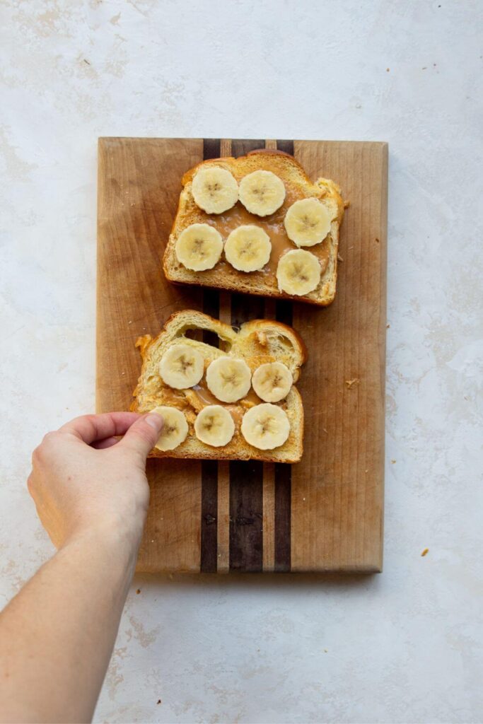 adding banana slices on top of the peanut butter bread