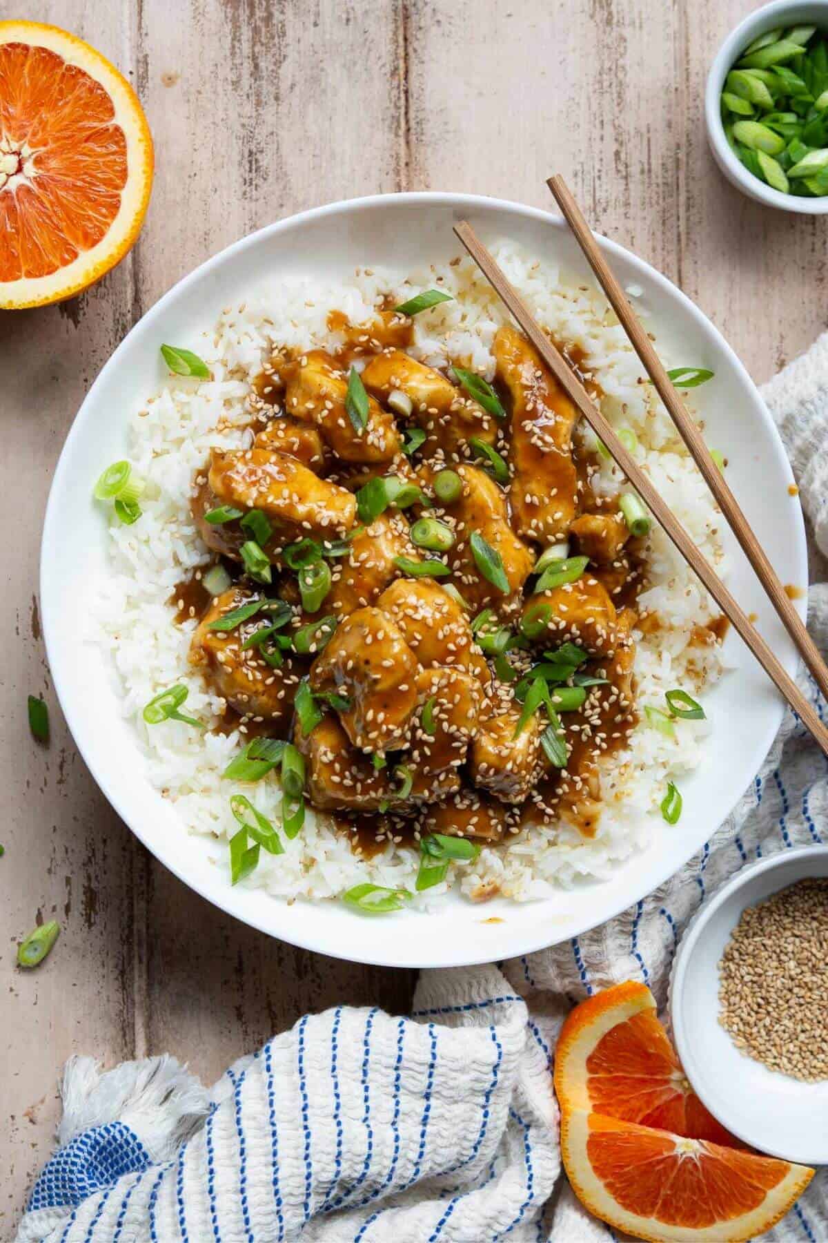 Healthy, sticky, and crispy air fryer orange chicken on a bed of rice with sesame seeds and green onion.