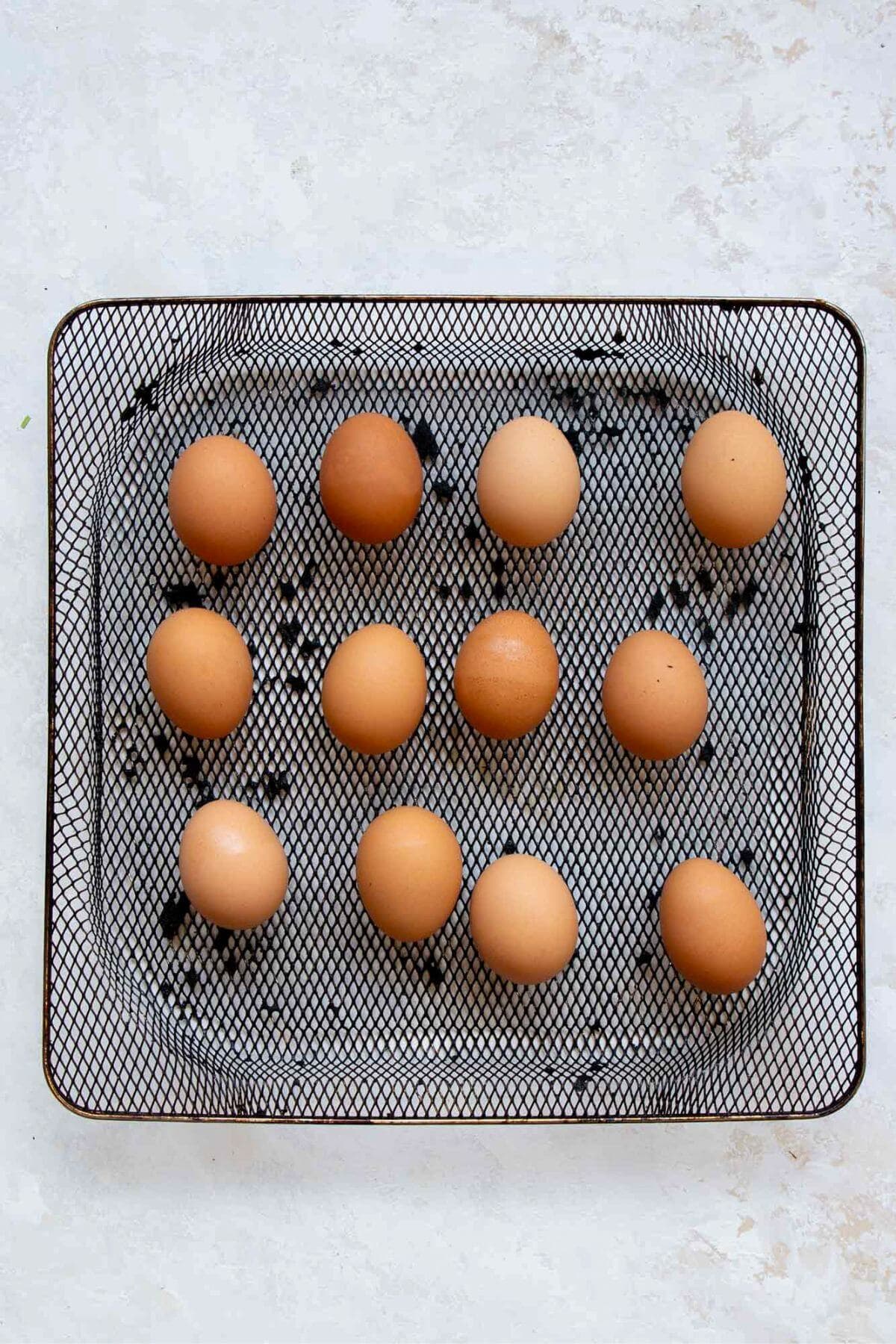 Raw eggs arranged in a single layer in an air fryer basket.