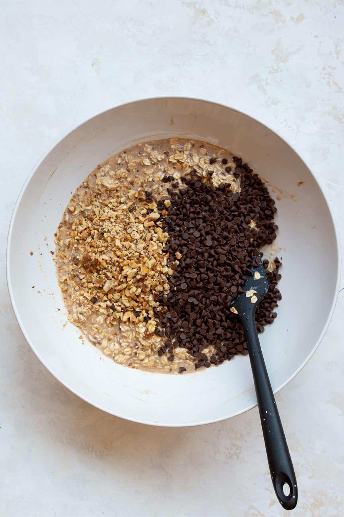Adding walnuts and chocolate chips to vegan baked oatmeal batter.