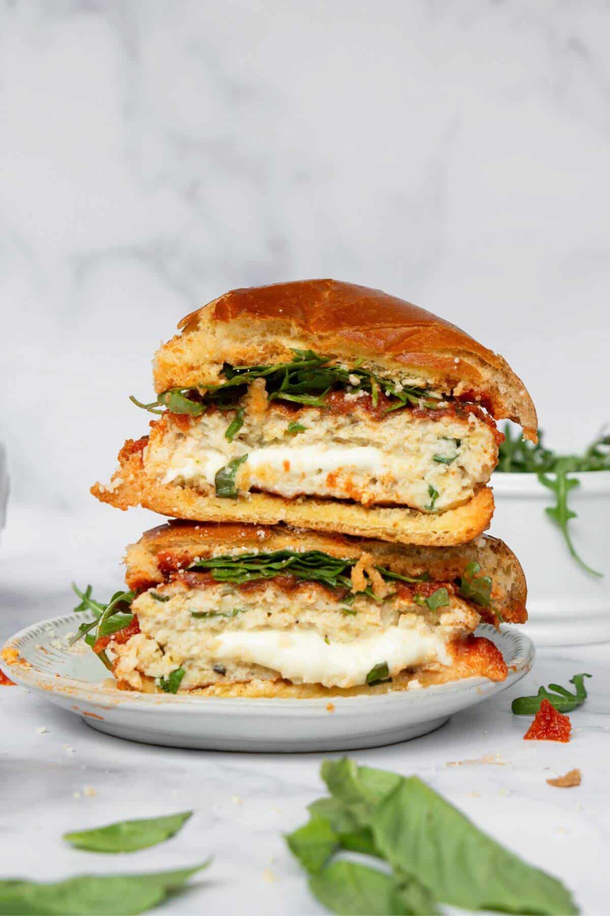Stuffed chicken parmesan burger cut in half and stacked, showing the melted mozzarella center with marinara, arugula, and fresh basil.