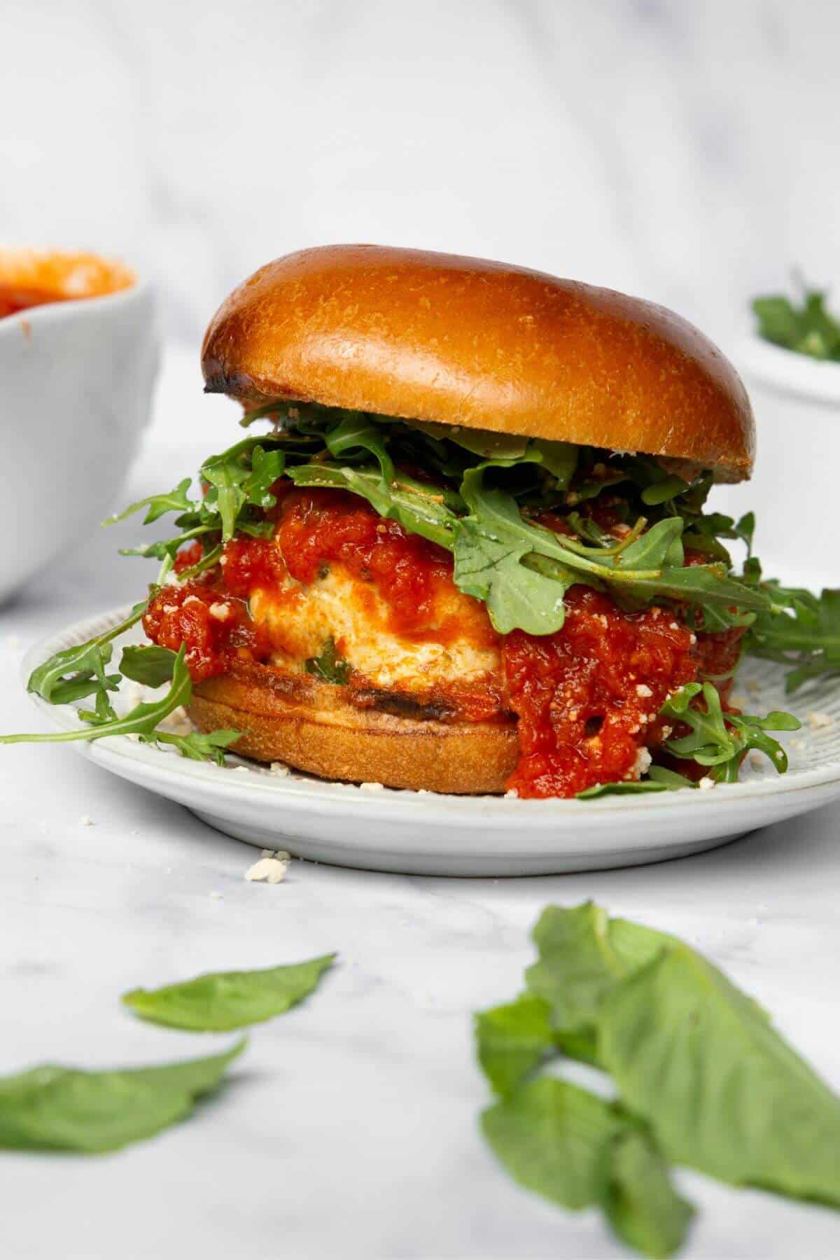 Stuffed chicken parm burger on a brioche bun with marinara sauce and arugula.