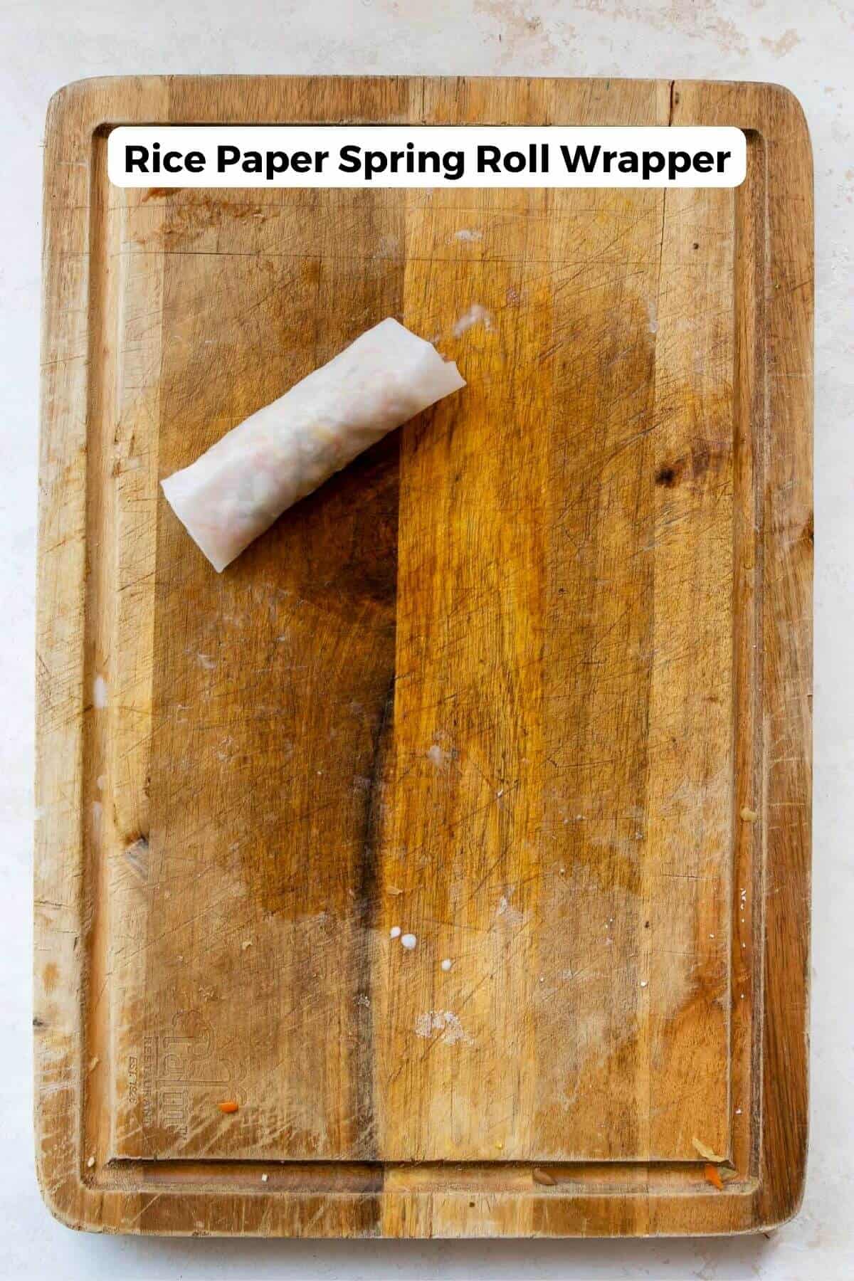 Finished rolled rice paper spring roll on a wooden cutting board.