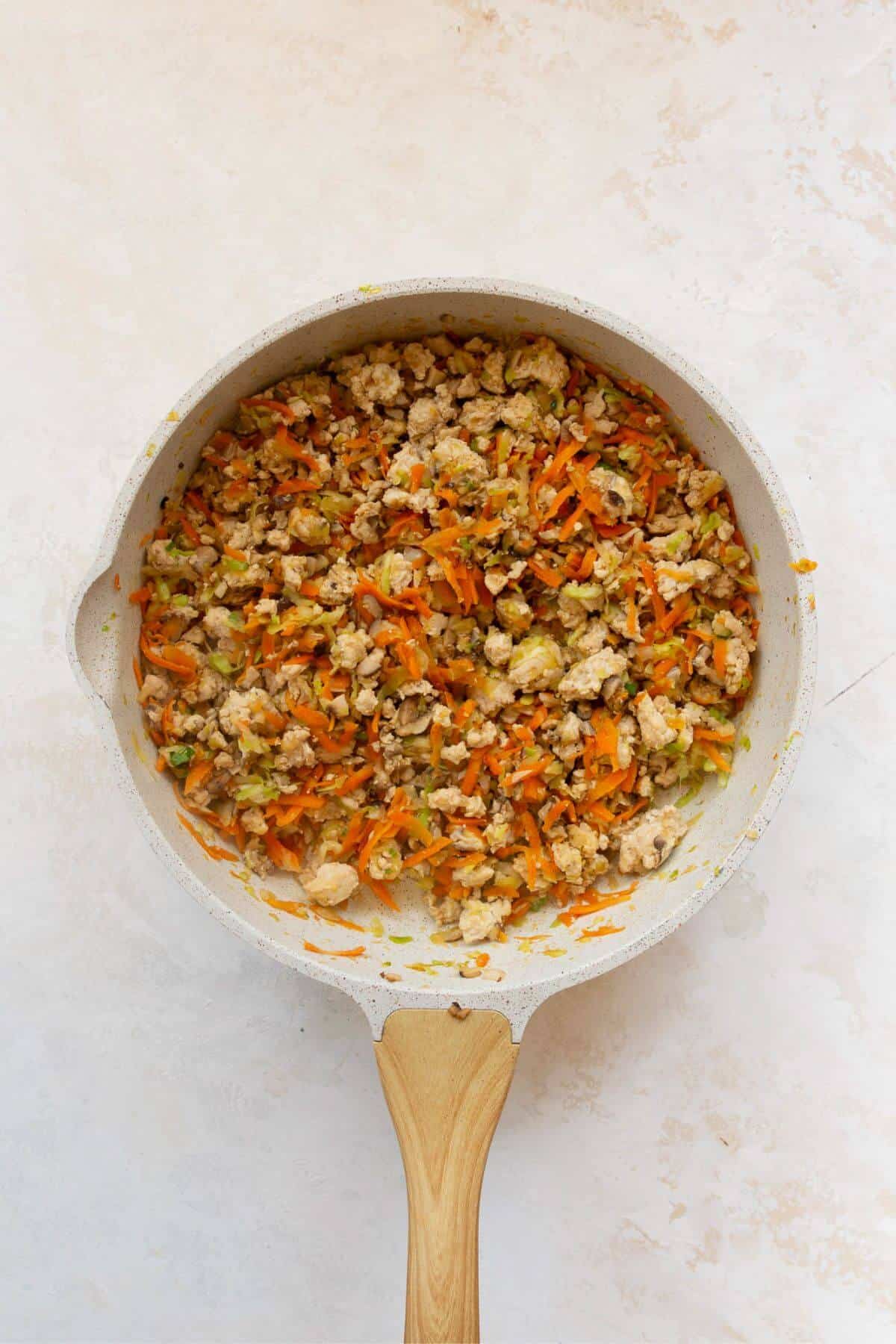 Finished spring roll filling with cabbage, carrots, and green onion in a skillet.